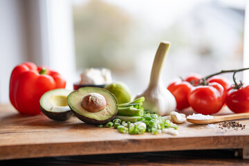 Healthy vegetables and fresh ingredients on wooden cutting board in front of bright kitchen window....