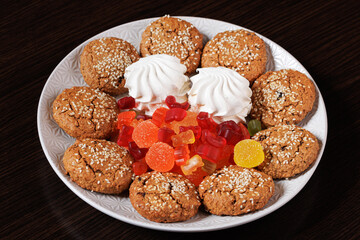A plate with sweets: cookies, marshmallows and marmalade on a dark table background. Angled view. Selective focus.