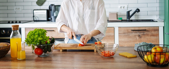 Woman cooking salad from green fresh vegetables while standing in the kitchen at home