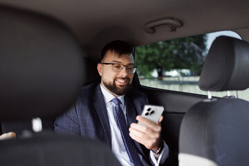 Positive spaniard businessman holding smartphone while sitting car. Man suit beard glasses modern phone. Solves issues related work road. Social networks. Modern technologies. Artificial intelligence