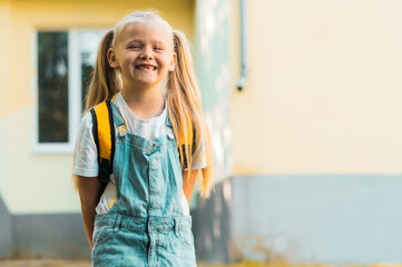 Cute smiling little girl with backpack on a greenery background. Education concept. First grader...