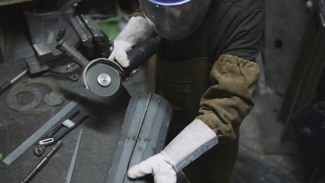 Top view of an artisan using a grinder cut and hammer to modify a piece of metal placed.