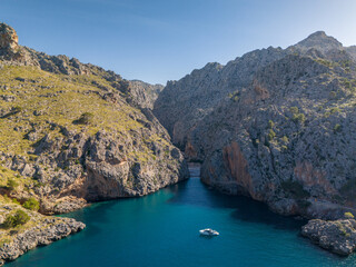 Boat in serene blue water surrounded by rocky mountains. Beach Sa Calobra, Mallorca