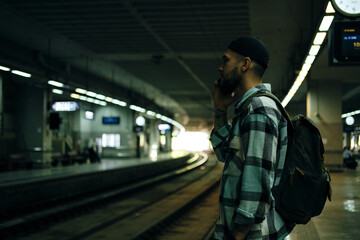 A young man travels alone with a backpack. The guy is standing on the platform, talking on the...