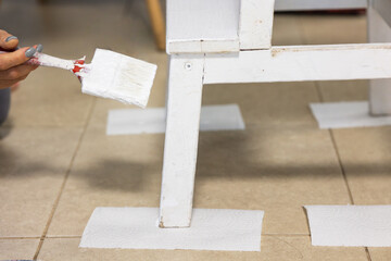 White chair with a side view is painted with a brush. A woman's hand is remodeling the furniture. Repair is a spring update. Cleaning and arrangement of the house. DIY is my hobbie 