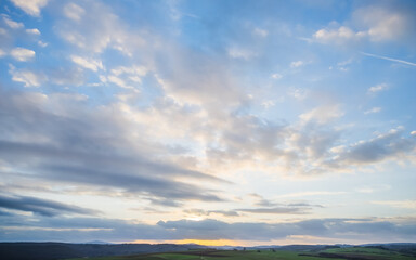 Obraz premium Scenic view of sunset over rural, green plains under cloudy sky