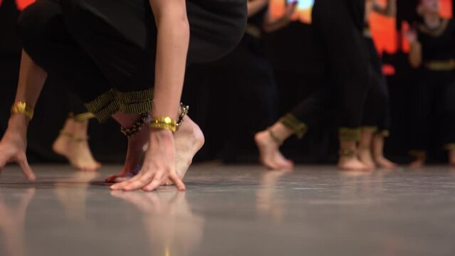 A crowd of girls dressed in traditional clothes and jewelry gracefully dance a traditional dance on stage. The legs are dancing dynamically. High quality 4k footage