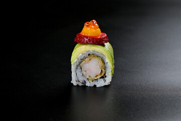 Piece of sushi on a black plate with drizzled sauce