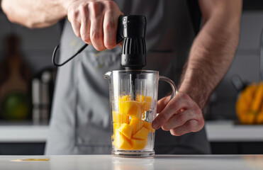 A man in an apron is using a hand blender to blend mango and apple juice