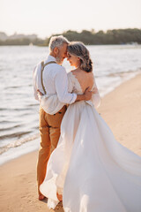 Senior newlyweds hug. Stylish couple of elderly newlyweds stand embracing on river bank.