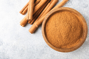Cinnamon powder in a bowl on a textured wooden background. Spicy spice for baking, desserts and drinks. Fragrant ground cinnamon. Cinnamon stick. Place for text. Copy space.