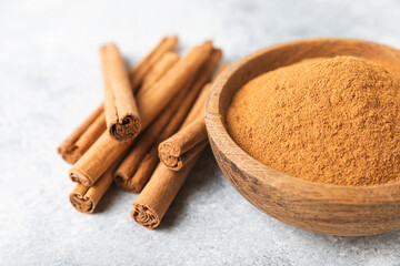 Cinnamon powder in a bowl on a textured wooden background. Spicy spice for baking, desserts and drinks. Fragrant ground cinnamon. Cinnamon stick. Place for text. Copy space.