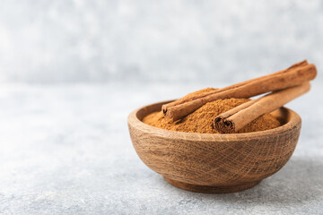 Cinnamon powder in a bowl on a textured wooden background. Spicy spice for baking, desserts and drinks. Fragrant ground cinnamon. Cinnamon stick. Place for text. Copy space.