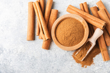 Cinnamon powder in a bowl on a textured wooden background. Spicy spice for baking, desserts and drinks. Fragrant ground cinnamon. Cinnamon stick. Place for text. Copy space.