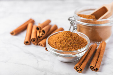 Cinnamon powder in a bowl on a textured wooden background. Spicy spice for baking, desserts and drinks. Fragrant ground cinnamon. Cinnamon stick. Place for text. Copy space.
