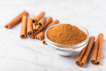 Cinnamon powder in a bowl on a textured wooden background. Spicy spice for baking, desserts and drinks. Fragrant ground cinnamon. Cinnamon stick. Place for text. Copy space.