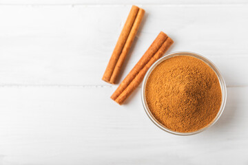 Cinnamon powder in a bowl on a textured wooden background. Spicy spice for baking, desserts and drinks. Fragrant ground cinnamon. Cinnamon stick. Place for text. Copy space.
