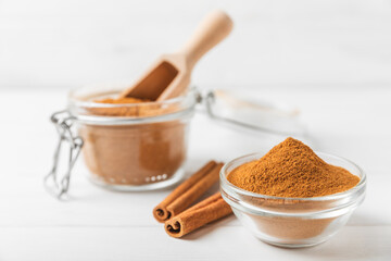 Cinnamon powder in a bowl on a textured wooden background. Spicy spice for baking, desserts and drinks. Fragrant ground cinnamon. Cinnamon stick. Place for text. Copy space.