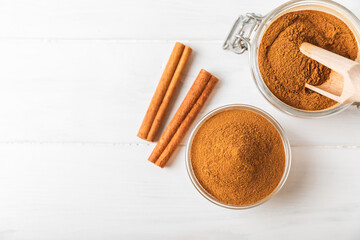 Cinnamon powder in a bowl on a textured wooden background. Spicy spice for baking, desserts and drinks. Fragrant ground cinnamon. Cinnamon stick. Place for text. Copy space.
