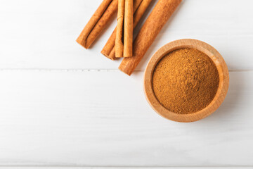 Cinnamon powder in a bowl on a textured wooden background. Spicy spice for baking, desserts and drinks. Fragrant ground cinnamon. Cinnamon stick. Place for text. Copy space.