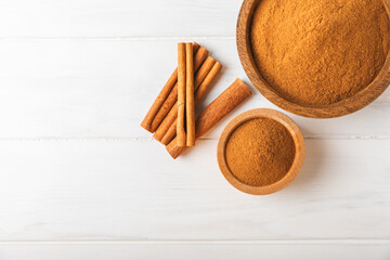 Cinnamon powder in a bowl on a textured wooden background. Spicy spice for baking, desserts and drinks. Fragrant ground cinnamon. Cinnamon stick. Place for text. Copy space.