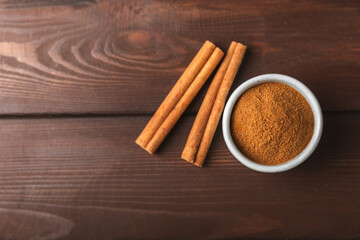 Cinnamon powder in a bowl on a textured wooden background. Spicy spice for baking, desserts and drinks. Fragrant ground cinnamon. Cinnamon stick. Place for text. Copy space.