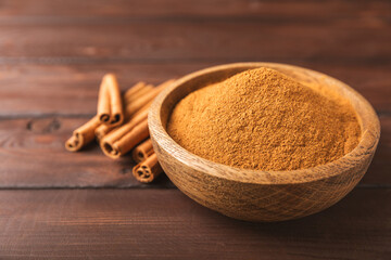 Cinnamon powder in a bowl on a textured wooden background. Spicy spice for baking, desserts and drinks. Fragrant ground cinnamon. Cinnamon stick. Place for text. Copy space.