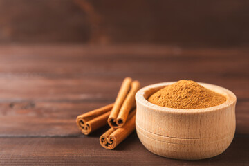 Cinnamon powder in a bowl on a textured wooden background. Spicy spice for baking, desserts and drinks. Fragrant ground cinnamon. Cinnamon stick. Place for text. Copy space.