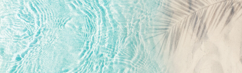 abstract empty sand beach from above with palm leaf shadow over transparent turquoise water wave, sunny background concept banner with copy space for travel and summer vacation outdoors
