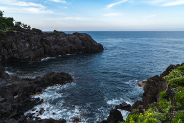 Obraz premium A beautiful coastal area in eastern part of Japan. A clear blue sky and an orange sunrise reflects on the sea water. A big rock formation in the coast line. Island from the distance.