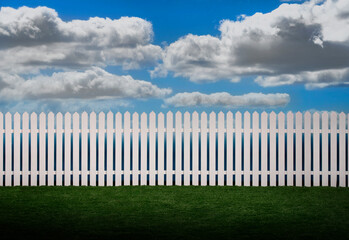 White picket fence with green grass and fluffy clouds in the background