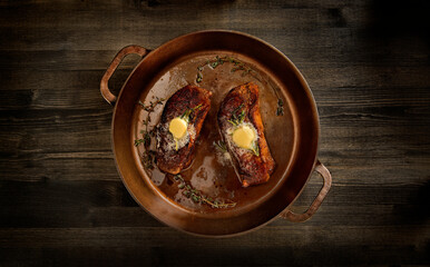 Top view of two appetizing striploin steaks cooked in a cast iron pan with butter and Rosemary herbs