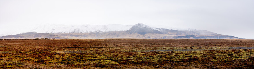 Fototapeta premium Vast field with snow-capped mountains in the background. Iceland