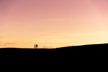 Couple in the distance silhouetted against the backdrop of the sky at sunset