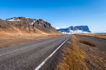 Country road with majestic cliffs in the background. Iceland