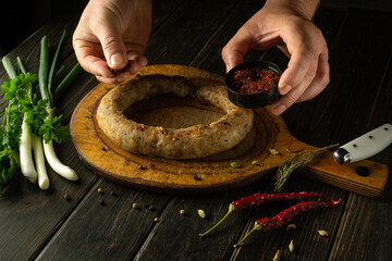 The chef hands add aromatic spices to the meat sausage on the cutting board. The concept of...