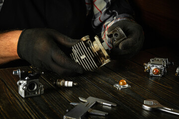Hands of a craftsman close-up at a work table in a workshop repairing an old engine of a gas mower...