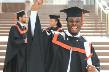 Happy graduate. Happy African man in graduation gowns holding diploma and smiling while his friends standing in the background