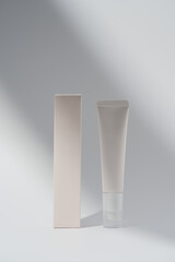 Mockup cream tube and box in shadow on blank background. Modern cosmetic presentation