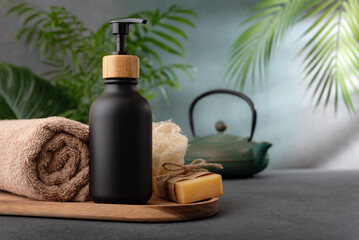 A black dispenser bottle of lotion or shower gel for body care product mock-up in tropical spa interior