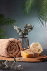 A wooden tray with a towel, soap, and a vase of eucalyptus