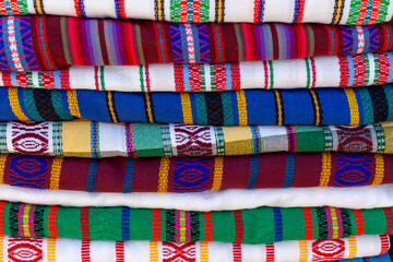 Close up of a pile of traditional, colorful, handmade textiles from El Salvador. Abstract stack of folded fabric, geometric, ethnic, background texture detail.