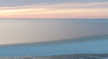 Sunset colored panoramic view of the calm seabay with the edge of the cracked sea ice and open water
