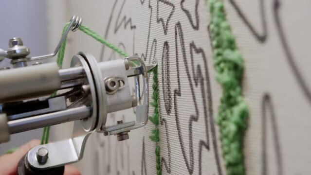 Close-up shot of a tufting gun, applying yarn to fabric with a unique pattern, is shown in the process of creating a rug using your own hands. Close up. Slow motion. 4k.