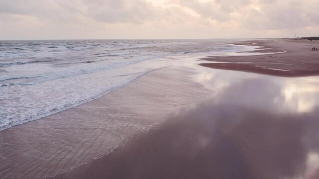 4K aerial view of ocean waves crashing on beach shore during cloudy day at Mandvi, Kutch, India. Calm coastline with sandy beach. Summer vacation, beach holidays concept. Travel and tourism background