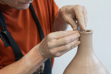 Close-up of a potter's hands making a ceramic vase on a potter's wheel. 
