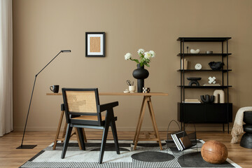 Creative composition of cozy workplace with mock up poster frame, wooden desk, rattan chair, black...
