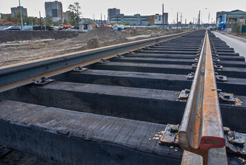 Naklejka premium Laying rails with wooden sleepers on ballast. Laying of the railway track. Repair and construction of roads. Railway tracks. Technologies and communications for transportation.