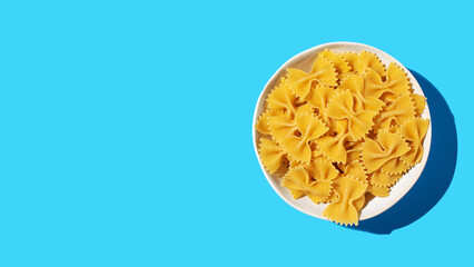 Uncooked bow tie pasta, farfalle in a white bowl on a vibrant blue background, perfect for culinary concepts. Copy space