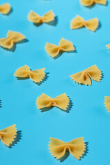 Naklejka premium Uncooked bow tie pasta, farfalle scattered on a blue background in a decorative pattern